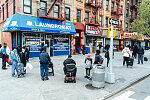 Laundromat with line of people outside, wearing masks, and spaced a few feet apart for social distancing. Harlem, New York City