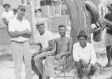 Men seated and standing in front of a tree in the dirt yard of a house in Newtown, a neighborhood in Montgomery, Alabama.