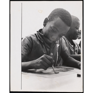 Close-up of a boy holding a brush in his mouth while working on a painting for his art class at the Boys' Clubs of Boston