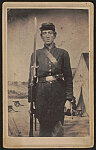 [Private George M. Stevens of Co. H, 9th New Hampshire Infantry Regiment in uniform with bayoneted rifle in front of painted backdrop showing military camp]