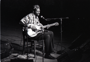 Taj Mahal in concert at Northfield, Mass.: Taj Mahal seated, playing steel guitar