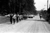 Edward Rudolph leading marchers down an unpaved road in Prattville, Alabama, during a demonstration sponsored by the Autauga County Improvement Association.