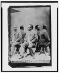 Thumbnail for [Unidentified African American man posed, full-length, seated, facing left, in front of mirrors, which reflect four mirror images of him]