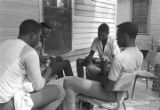 Four young men playing cards on the front porch of a clapboard house in Newtown, a neighborhood in Montgomery, Alabama.