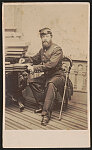 [Unidentified soldier in Union uniform with sword seated writing at desk in front of painted backdrop showing balustrade]