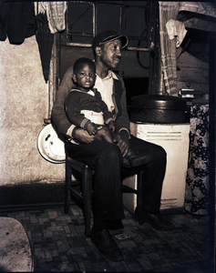 Man holding child on his lap, bllack-and-white photonegative.