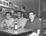 Three friends, two Asian-American, one African-American, sitting at a table drinking beer and socializing at the Banquet Cafe and Tavern, 1239 Jackson St., Seattle, ca. 1950's