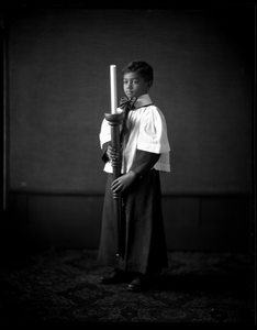 R.B. Thomas as a young boy, dressed as an acolyte, holding candle. Black-and-white photonegative.
