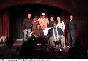 Performer, man, and Curtis King sitting on stage with three women and three men standing