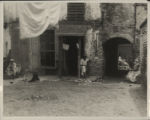 African-American tenement courtyard. Woman washing, man and woman smoking.