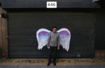 Unidentified man in a black cap posing in front of a mural depicting angel wings