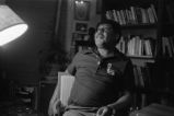 Gaines seated talking in front of bookshelves (EGP-9 #292)