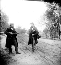 Two men standing near the old Alameda Avenue bridge one is playing a mandolin