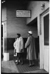 [Two African American women standing near a sign reading "Waiting Room Colored Intrastate Passengers" at a Greyhound bus station, Atlanta, Georgia]