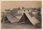 [Two small tents, with wood frame buildings in the background]