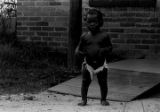 Baby standing in the yard in front of a brick house in Newtown, a neighborhood in Montgomery, Alabama.