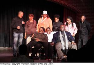 Performer, man, and Curtis King sitting on stage with three women and three men standing