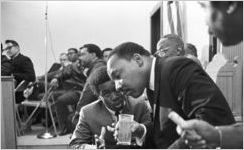 Martin Luther King, Jr., seated and speaking to a young man during a meeting at Maggie Street Baptist Church in Montgomery, Alabama.