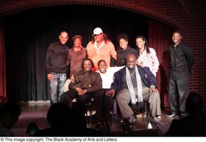 Performer, man, and Curtis King sitting on stage with three women and three men standing