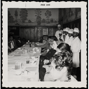 Several Boys' Club members wearing chef outfits and standing behind the guests during a Boys' Club Inaugural Dinner