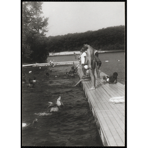 A swimming supervisor stands on the dock watching a group of children