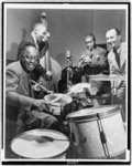 [Louis Armstrong on trumpet, Warren Dodds on drums and George Foster on the double bass during broadcast of "This is Jazz" radio show, directed by Rudi Blesh (far right)]