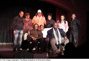 Performer, man, and Curtis King sitting on stage with three women and three men standing