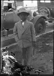 Portrait of boy in bow tie and suit in yard with automobiles in the background