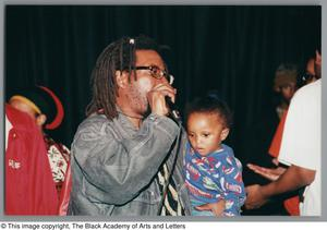 Photograph of a man holding onto a child and microphone