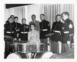 Duke Ellington with 7 U.S. Marines standing behind an unknown woman seated at a drum set in Baghdad, Iraq during 1963 State Department Tour : black-and-white photoprint