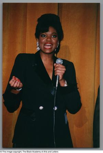 Medium shot of a woman, with her mouth open, holding a microphone and curling her right hand