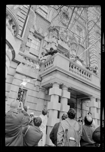 Student leaps across balcony over entrance to administration building at Boston University while others hoisted portable mike