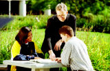 Rev. Robert A. Wild, S.J., poses with two students seated at outdoor tables on the Marquette campus, 1996