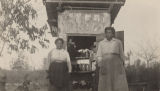 Two African American woman standing outside a small wooden outbuilding filled with jars of preserves, in rural Madison County, Alabama.