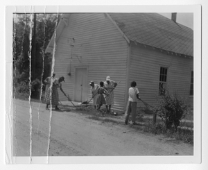 Photograph of African American men and women raking land by a wooden building, Clarkesville, Habersham County, Georgia, 1953