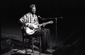 Taj Mahal in concert at Northfield, Mass.: Taj Mahal seated, playing steel guitar