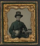 [Unidentified young soldier in Union uniform and plumed Hardee hat with plain gauntlets and revolver sitting next to table with books]