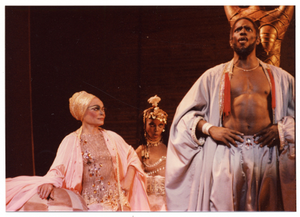 Performance picture of Eartha Kitt (wearing a gold turban), a man, and a woman (in the background)]. [color photoprint