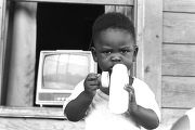 Baby holding a bottle on the front porch of a clapboard house in Newtown, a neighborhood in Montgomery, Alabama.