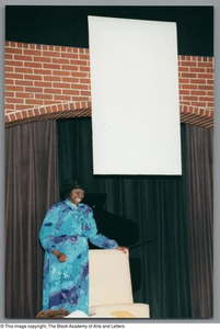 Photograph of Mzuri with her hand on a chair