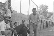 Men and children sitting in front of a fence on the edge of the field during a boys' baseball game, probably in Montgomery, Alabama.