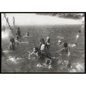 A group of children splash around in the water by a rope line