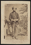 [Unidentified soldier in Union cavalry uniform with saber in front of painted backdrop showing military camp]