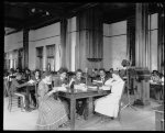 [Interior view of library reading room with male and female students sitting at tables, reading, at the Tuskegee Institute]