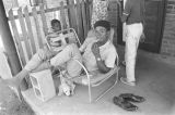 Man sitting on a lawn chair on the front porch of a brick house in Newtown, a neighborhood in Montgomery, Alabama.