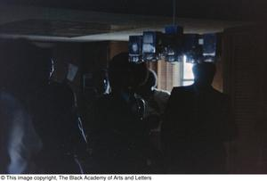 Underexposed photograph of a crowd of people standing near a kitchen area