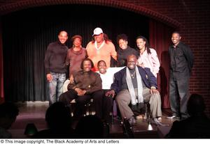 Performer, man, and Curtis King sitting on stage with three women and three men standing