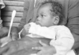 Baby held in a person's lap on the porch outside a house in Little Korea, a neighborhood in Birmingham, Alabama.