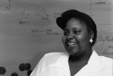 Jacqueline Hatter stands in front of a white board covered with diagrams, 1988