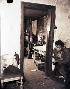 Shabby interior with two figures: girl on right, young boy in another room seen through doorway, photonegative